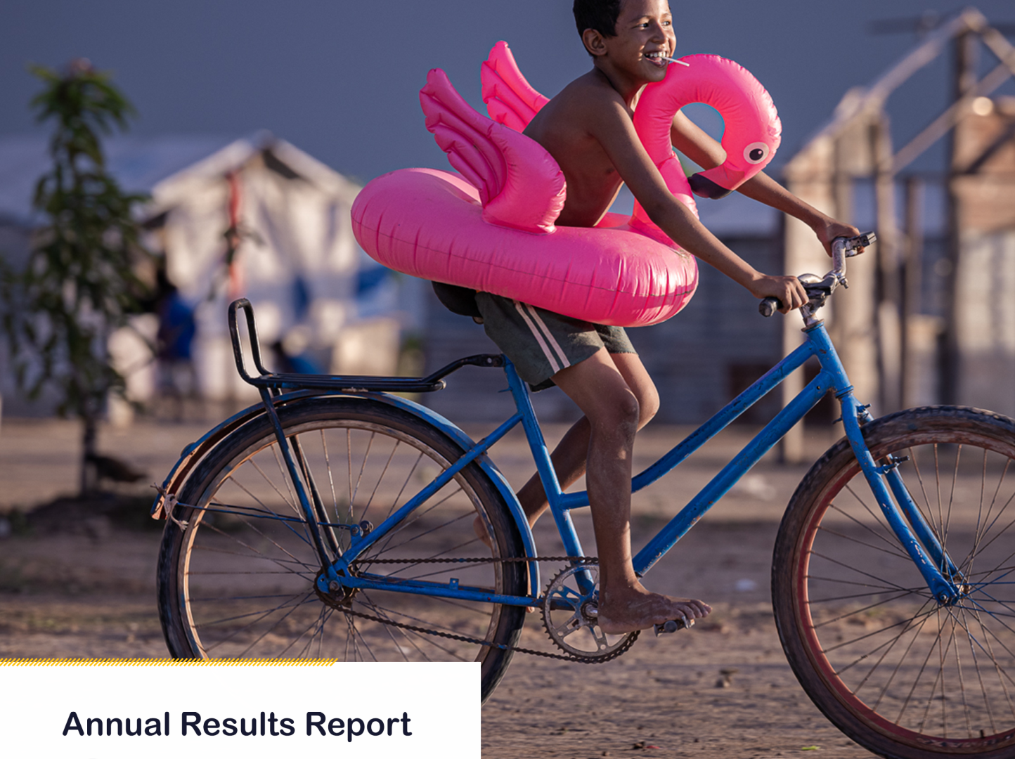 A photo of a report cover with a title - Annual Reports Report Guyana 2024. It has a photo of a boy on a bicycle with a pink inflatable flamingo around his waist. 