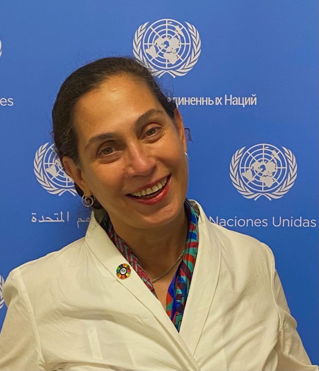 A woman smiling in front of a UN banner.