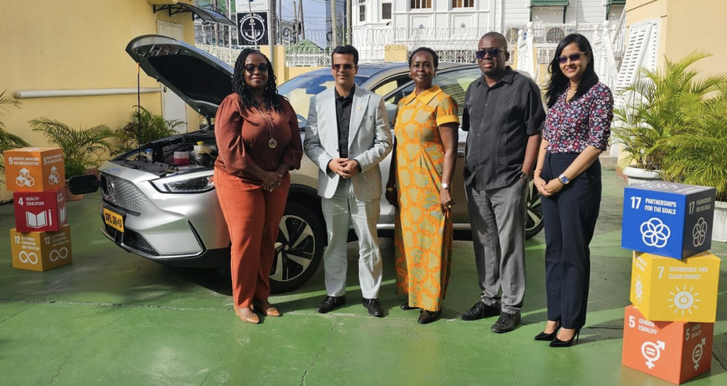 Two men and three women standing in front of an electric vehicle.