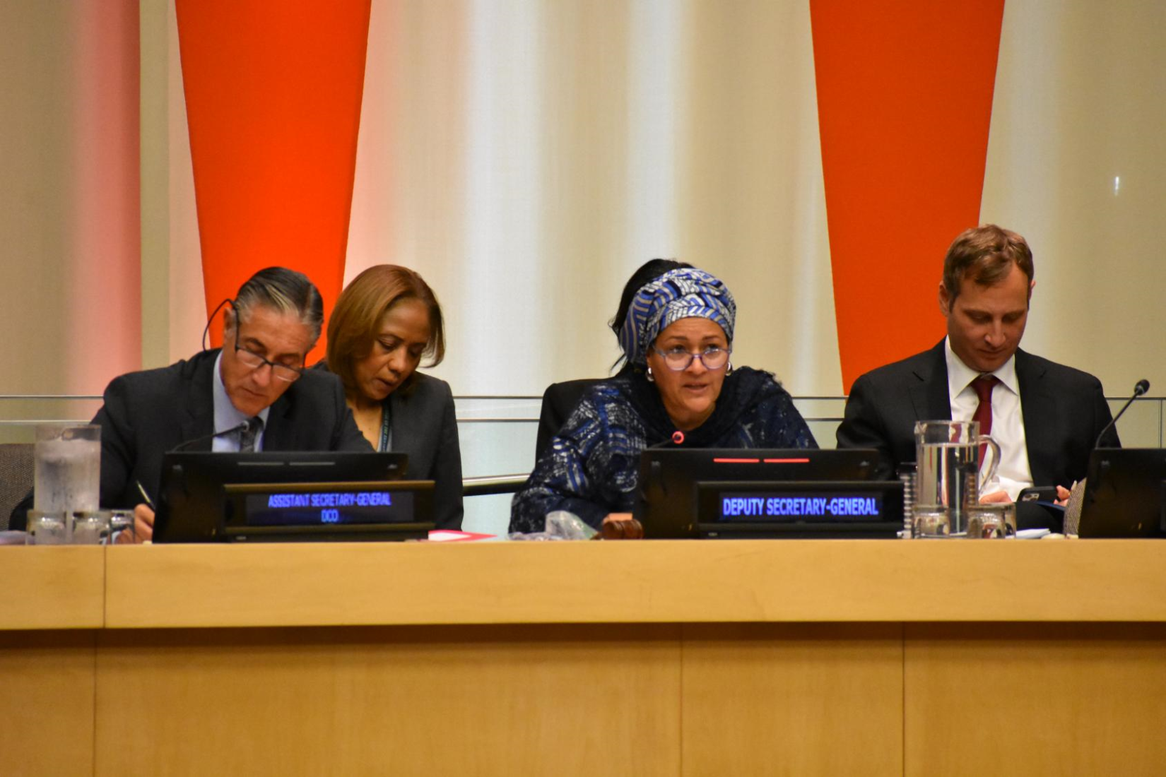 A woman seated speaking. Two persons are seated next to her and two behind her.