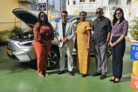 Two men and three women standing in front of an electric vehicle.