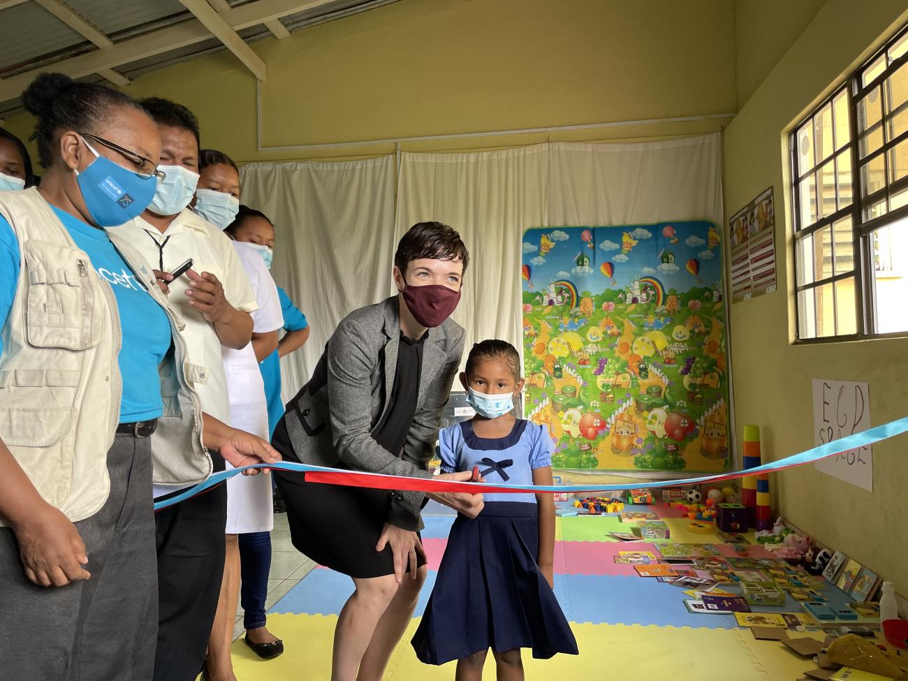 Executive Director of the Caribbean Regional Development Program, Global Affairs Canada, Sharon Peake assists a child to cut the ribbon to officially open the ECD space at the Annai Health Centre on Monday, 22 November 2021.