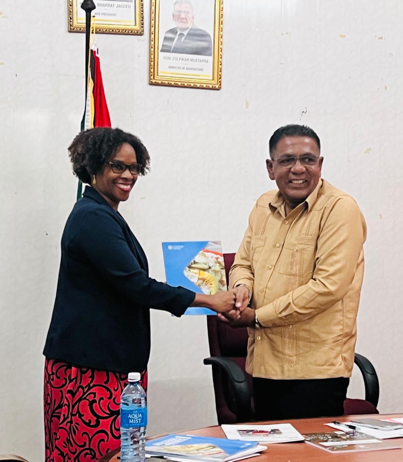 FAO Representative Dr. Gillian Smith hands over a manual to Guyana's Minister of Agriculture Zulfikar Mustapha