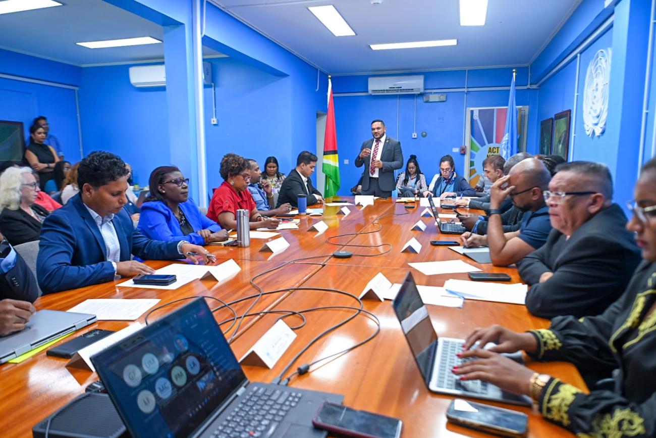 People seated around a table and Minister Bharrat is standing.