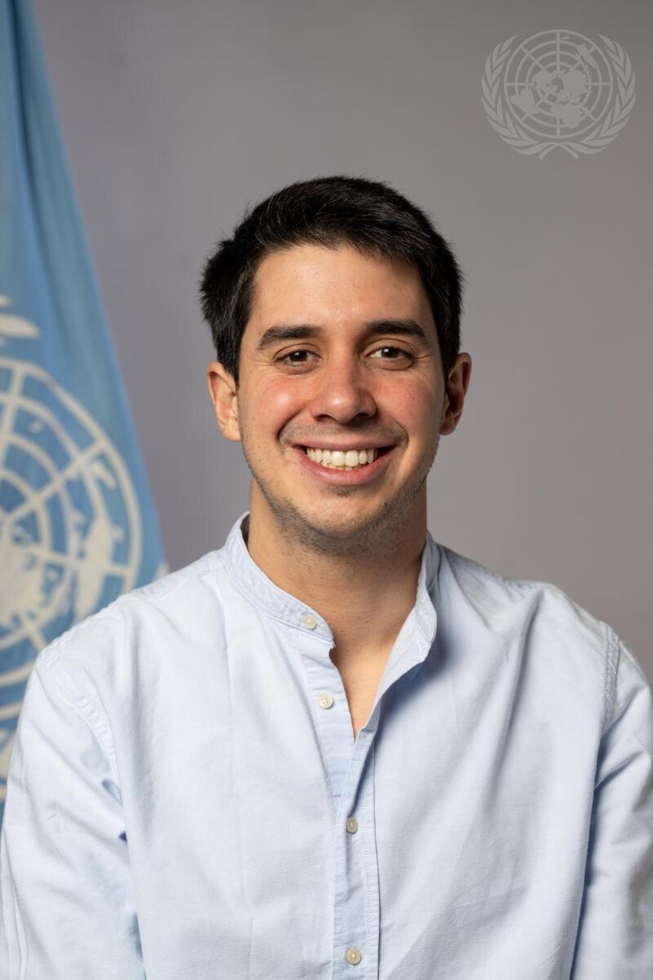 A photo of a young man smiling with a UN flag in the background.