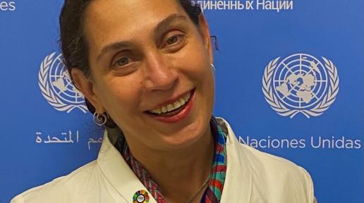 A woman smiling in front of a UN banner.