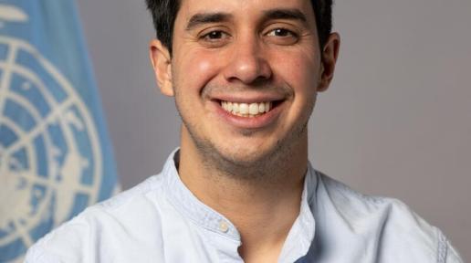 A photo of a young man smiling with a UN flag in the background.