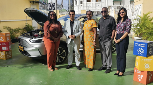 Two men and three women standing in front of an electric vehicle.