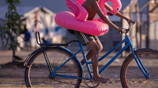 A photo of a report cover with a title - Annual Reports Report Guyana 2024. It has a photo of a boy on a bicycle with a pink inflatable flamingo around his waist. 